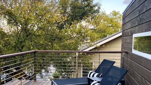 A deck with two lounge chairs and a table, surrounded by a metal railing.