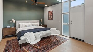 Um quarto moderno com uma cama grande, ventoinha no teto, mesa de cabeceira, cadeira, tapete e guarda-roupa.