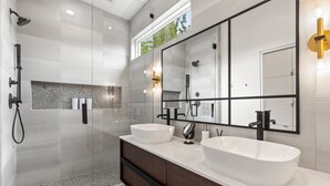 A modern bathroom with two large white sinks, a glass-enclosed shower, and a large mirror with black frames.