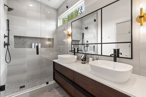 A modern bathroom with two large white sinks, a glass-enclosed shower, and a large mirror with black frames.