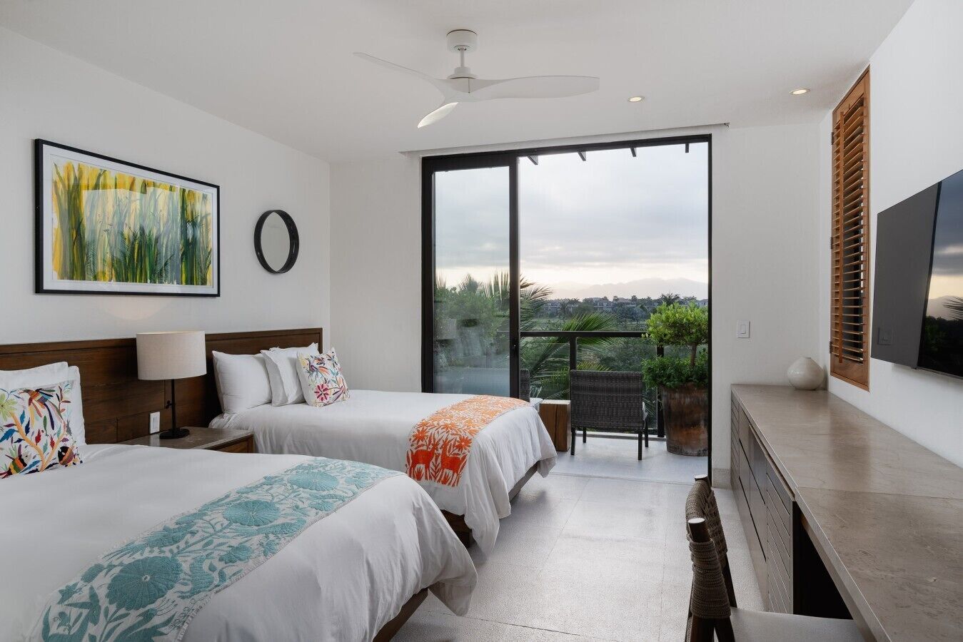 A modern hotel room with two beds, a balcony, a TV, and a large window with a view.