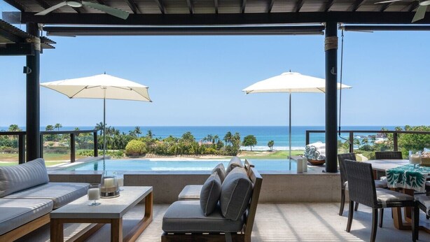 A covered outdoor seating area with a pool, two umbrellas, and a view of the ocean. - Condo Piscis in Las Marietas by Mita Residential. Golf Cart, Cook, Ocean View, Pool (Punta Mita)