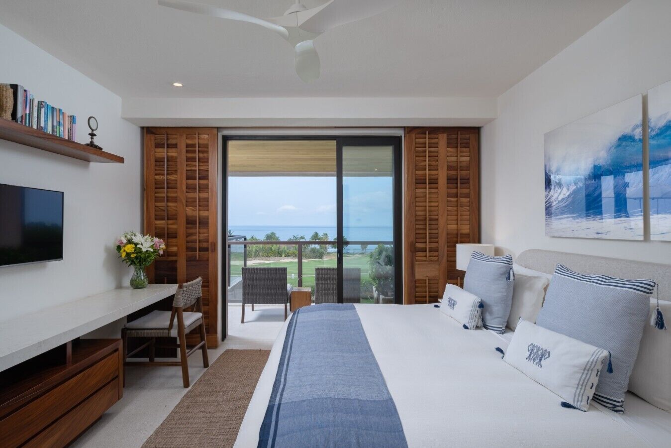 Una habitación de hotel moderna con una cama grande, un escritorio, un televisor y un balcón con vistas al océano.