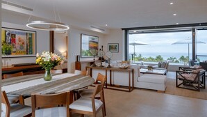 A modern interior with a dining area, seating, and a large window with a view. - Condo Piscis in Las Marietas by Mita Residential. Golf Cart, Cook, Ocean View, Pool (Punta Mita)