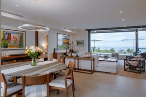 A modern dining area with a long table, chairs, and a vase of flowers.