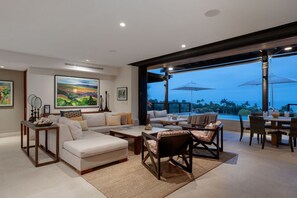 A modern living room with a sofa, coffee table, and chairs, a dining area with a table and chairs, and a large window overlooking a scenic view.