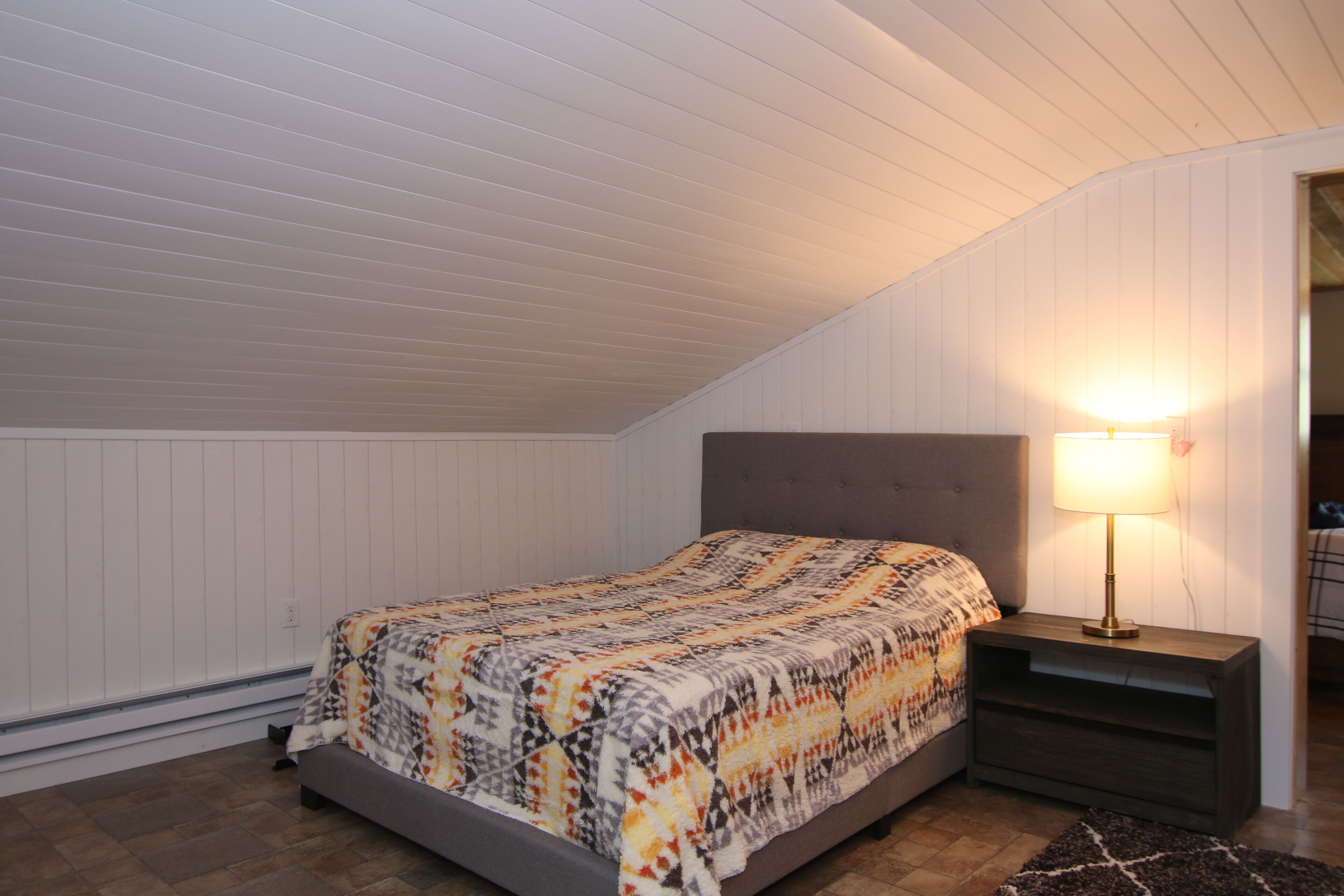 A bedroom with a bed, a nightstand with a lamp, and a wooden floor.