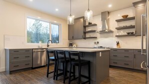 A modern kitchen with a large island, dark grey cabinets, and a window providing natural light.