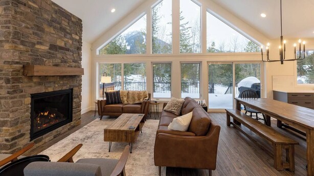 A spacious living room with a stone fireplace, large windows, and a high ceiling fan.