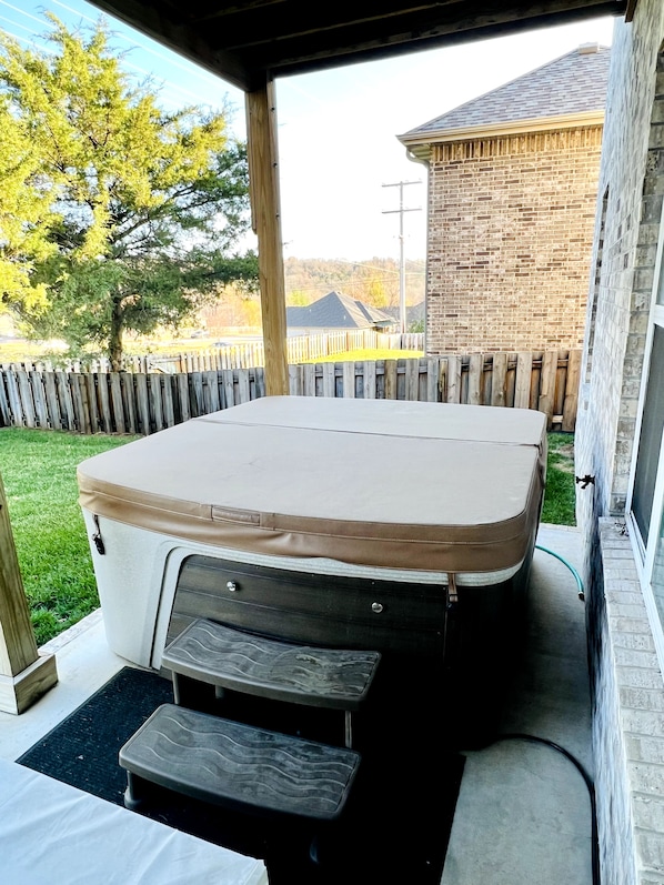 A covered outdoor hot tub with a beige cushion, a step-up platform, and a small table.
