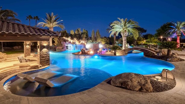 Une piscine agrémentée d’une cascade, entourée de palmiers et dotée d’une terrasse en pierre.