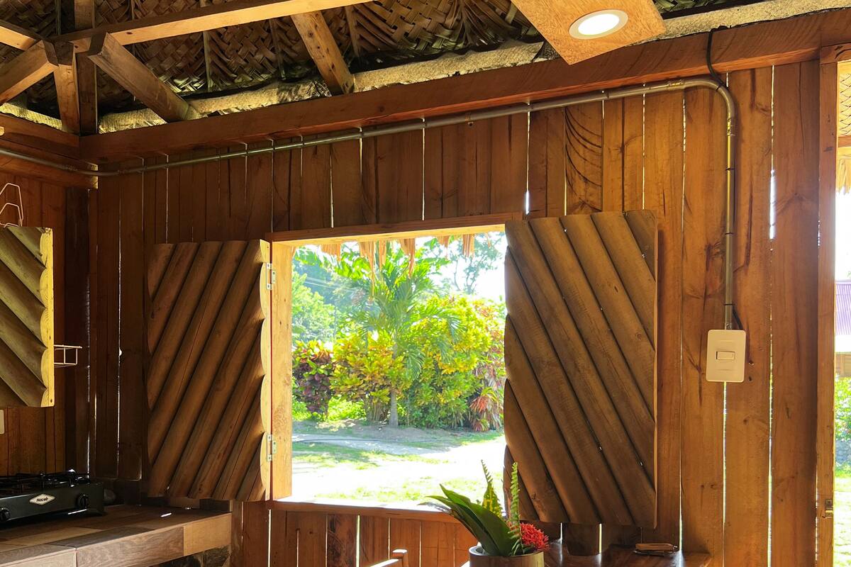 A wooden kitchen with a large window, a stone countertop, and a wooden table.