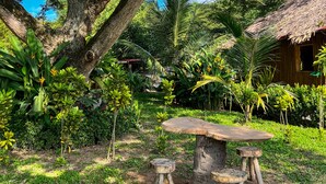 A rustic outdoor setting with a large tree, a thatched-roof hut, and a wooden table with stools. - Tayrona Cachaco River  (Santa Marta)