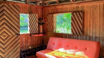 Een kamer met rieten dak, houten wanden, een rode bank en uitzicht op groen.