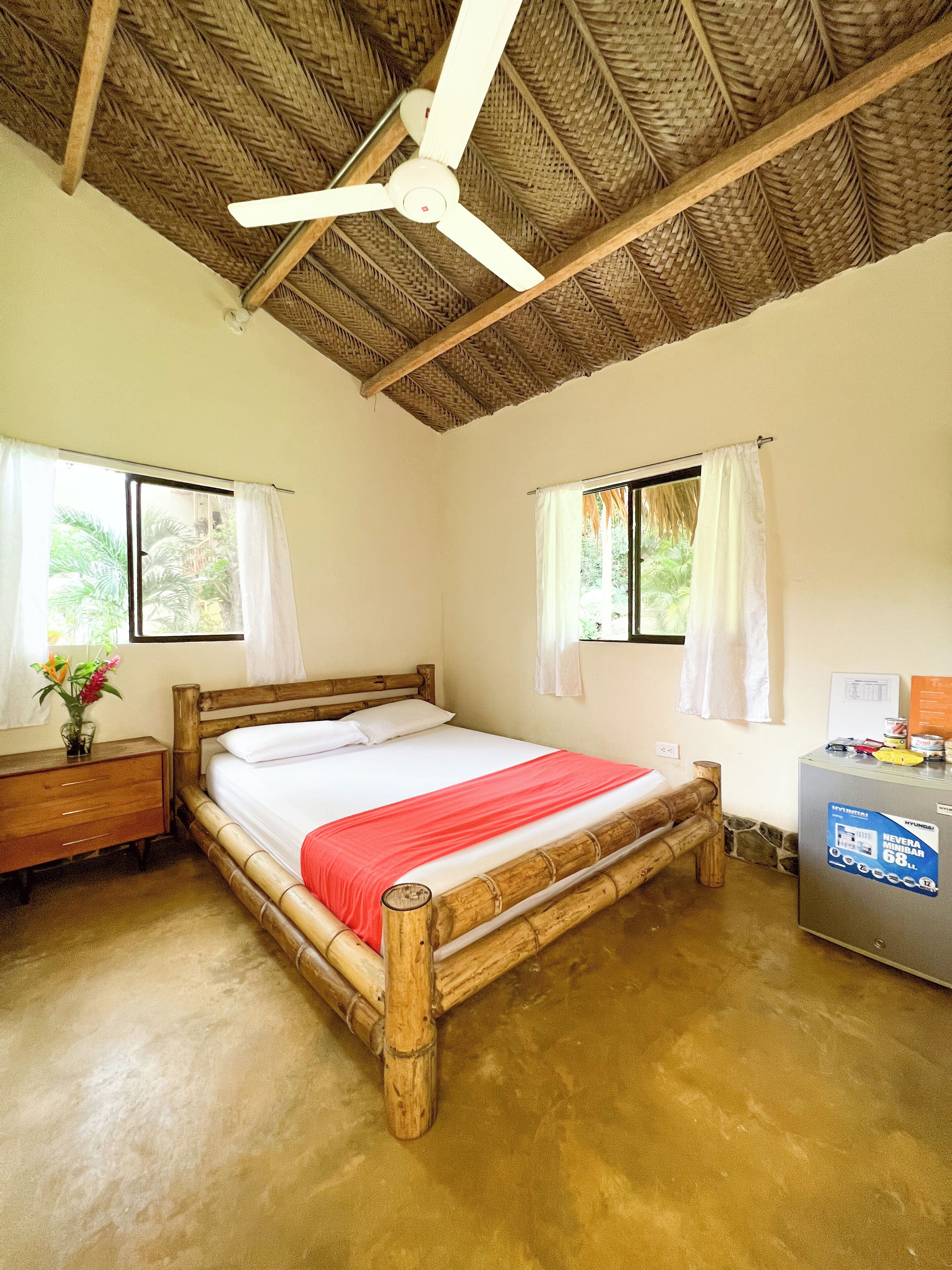 A room with a wooden bed, a ceiling fan, a nightstand, a dresser, and a window with curtains.