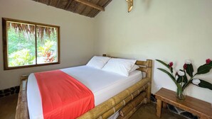 A room with a bed, a window with a view of greenery, a wooden headboard, and a bedside table with a vase of flowers. - Tayrona Cachaco River  (Santa Marta)