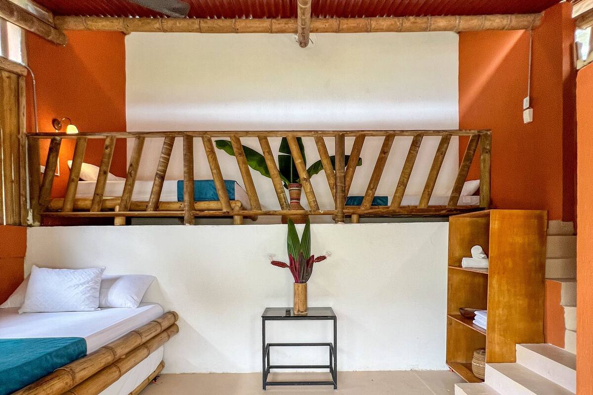 A room with a bed, a small table with a plant, a wooden shelf, and a staircase.