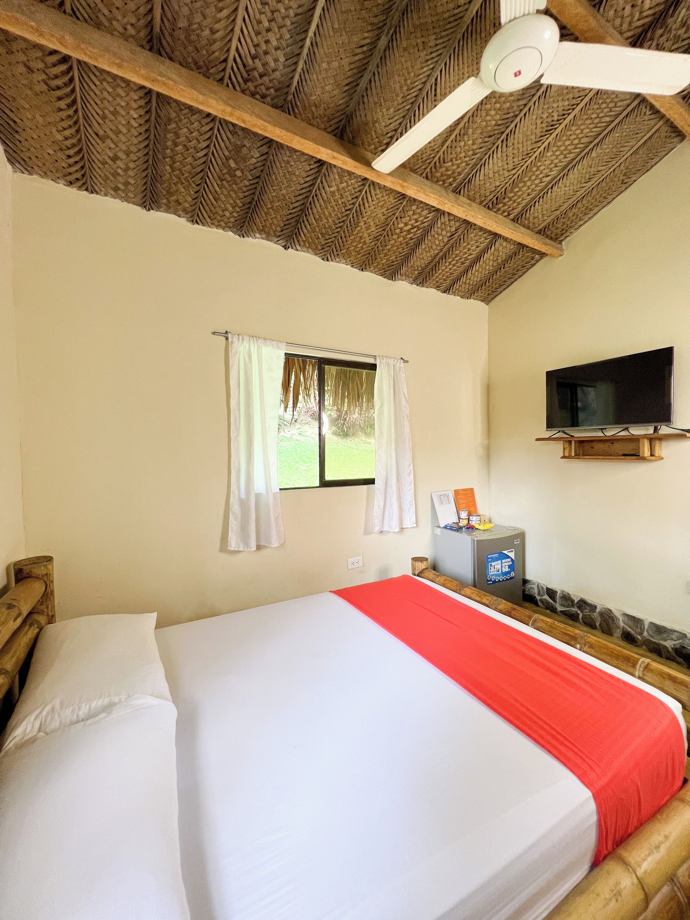 A hotel room with a bed, a television, a window with curtains, and a ceiling fan.