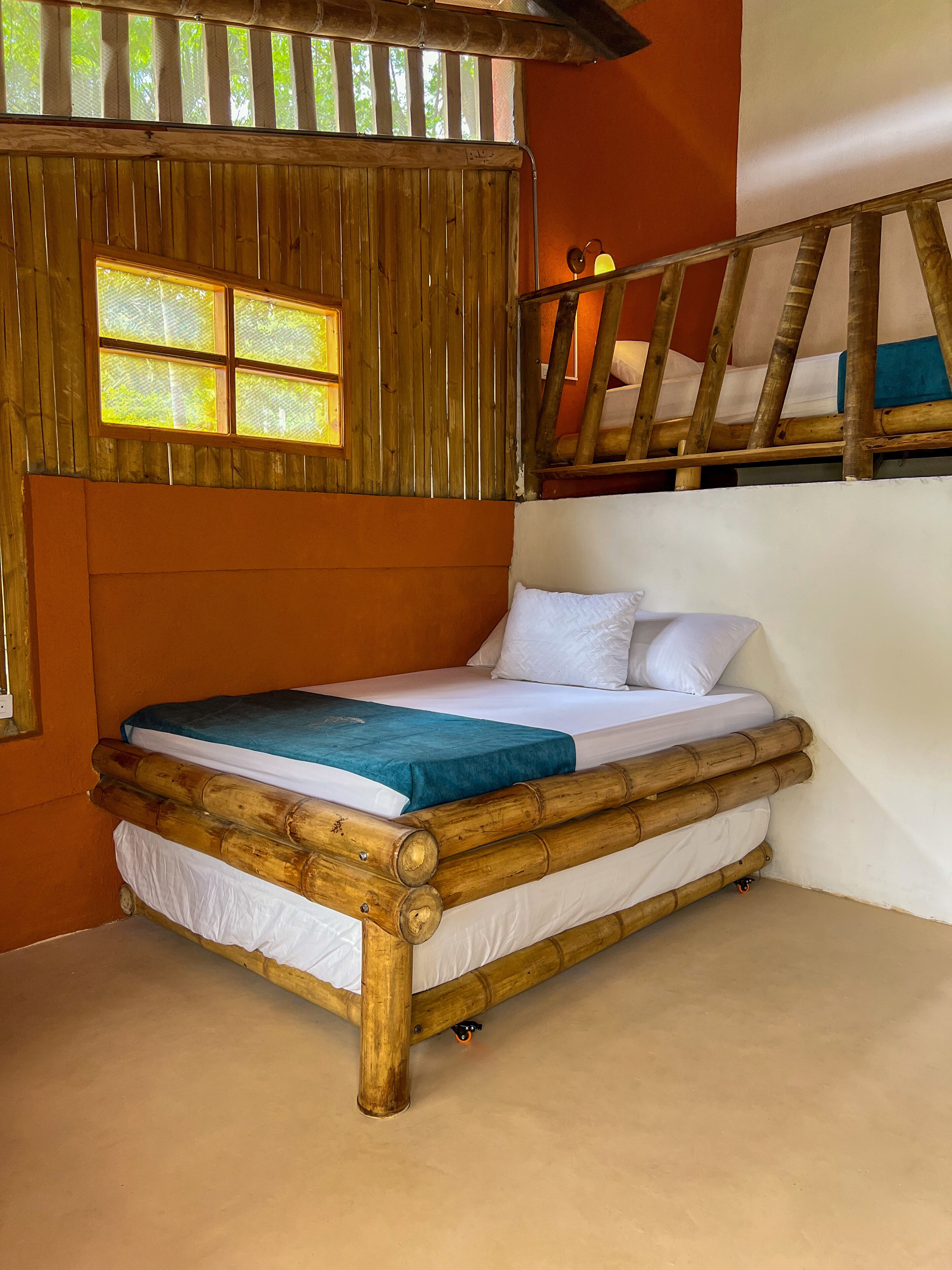 A bed with a wooden frame and white bedding, a window with a view of trees, and a wooden staircase.
