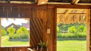 A wooden bar with a curved countertop, a hanging light fixture, and a view of a lush garden. - Tayrona Cachaco River  (Santa Marta)