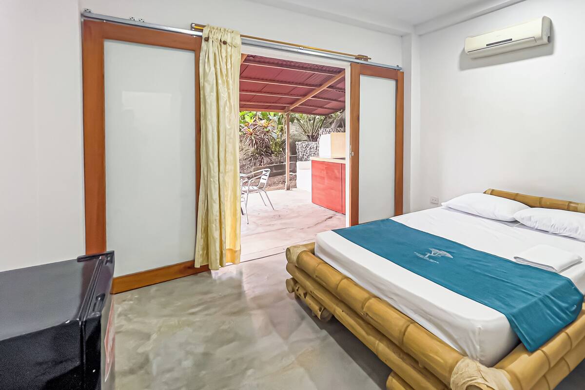 A room with a bed, a TV, and a sliding door leading to an outdoor area.