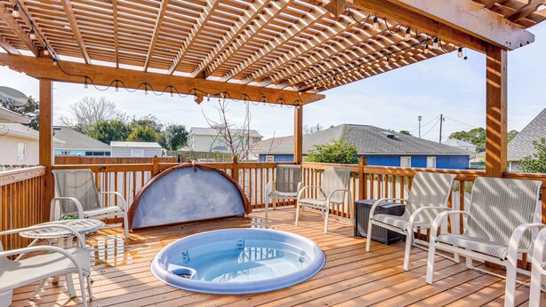 Eine Holzterrasse mit Whirlpool, weißen Korbstühlen und einer Pergola mit Lichterketten.