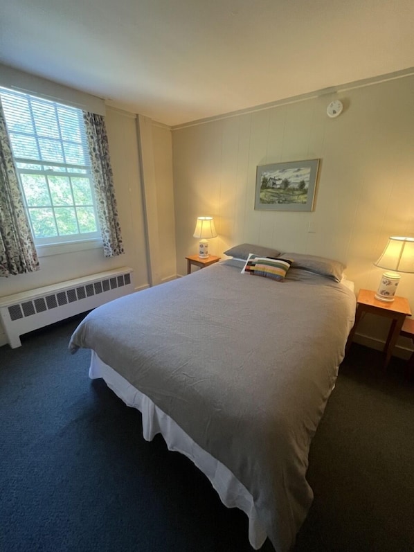 A bedroom with a large bed, two bedside tables with lamps, a radiator, and a window with curtains.