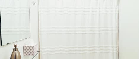 A bathroom with a white sink, a mirror, a shower curtain, and a bottle of soap.
