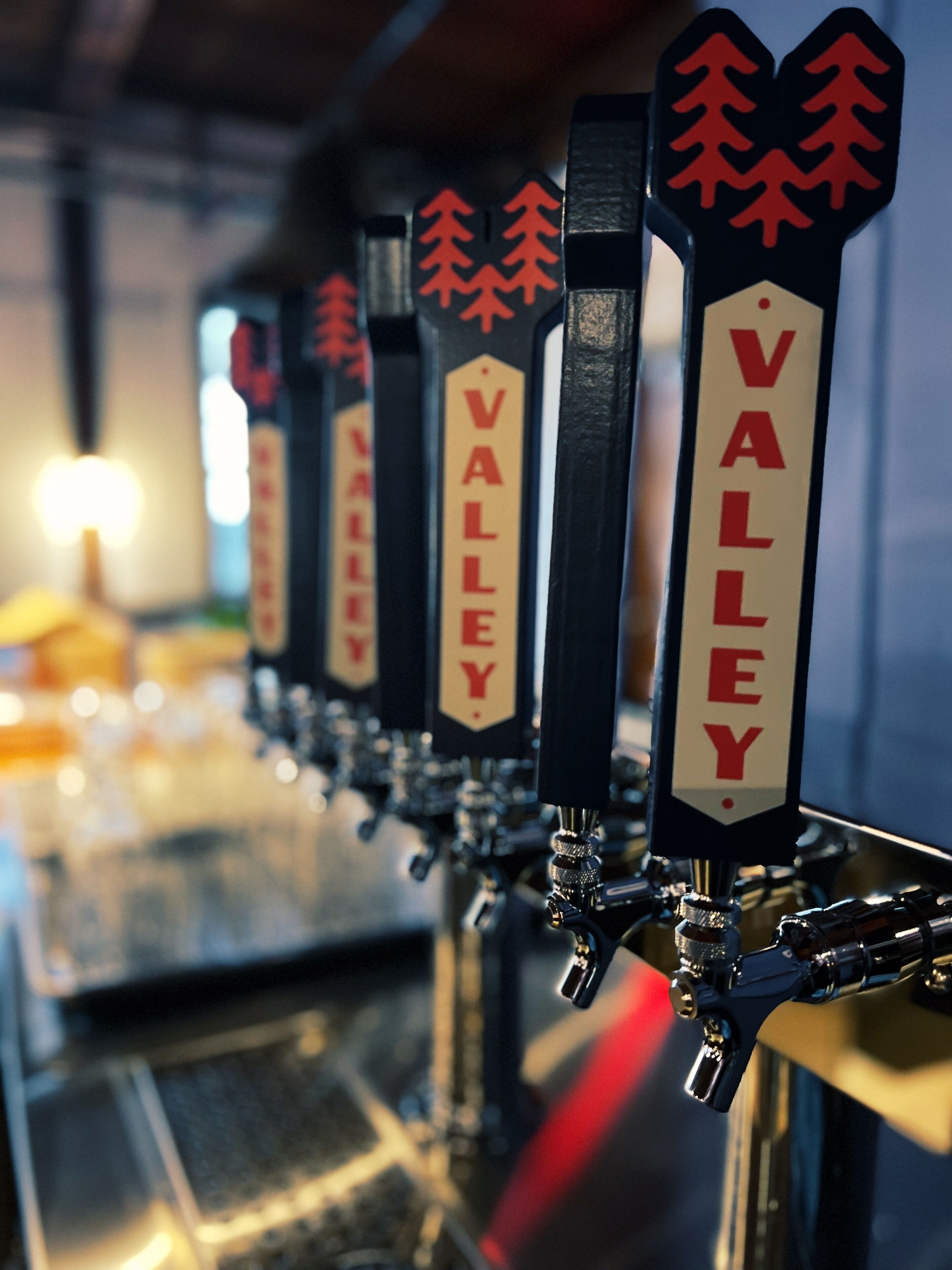 Una fila de grifos de cerveza con la etiqueta 'VALLEY' y un logotipo de árboles rojos.