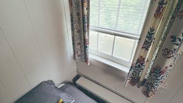 Una habitación pequeña con una cama individual, una ventana con cortinas florales y un radiador.