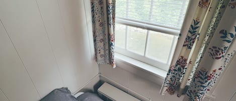 Une petite pièce avec un lit simple, une fenêtre ornée de rideaux à motifs floraux et un radiateur.