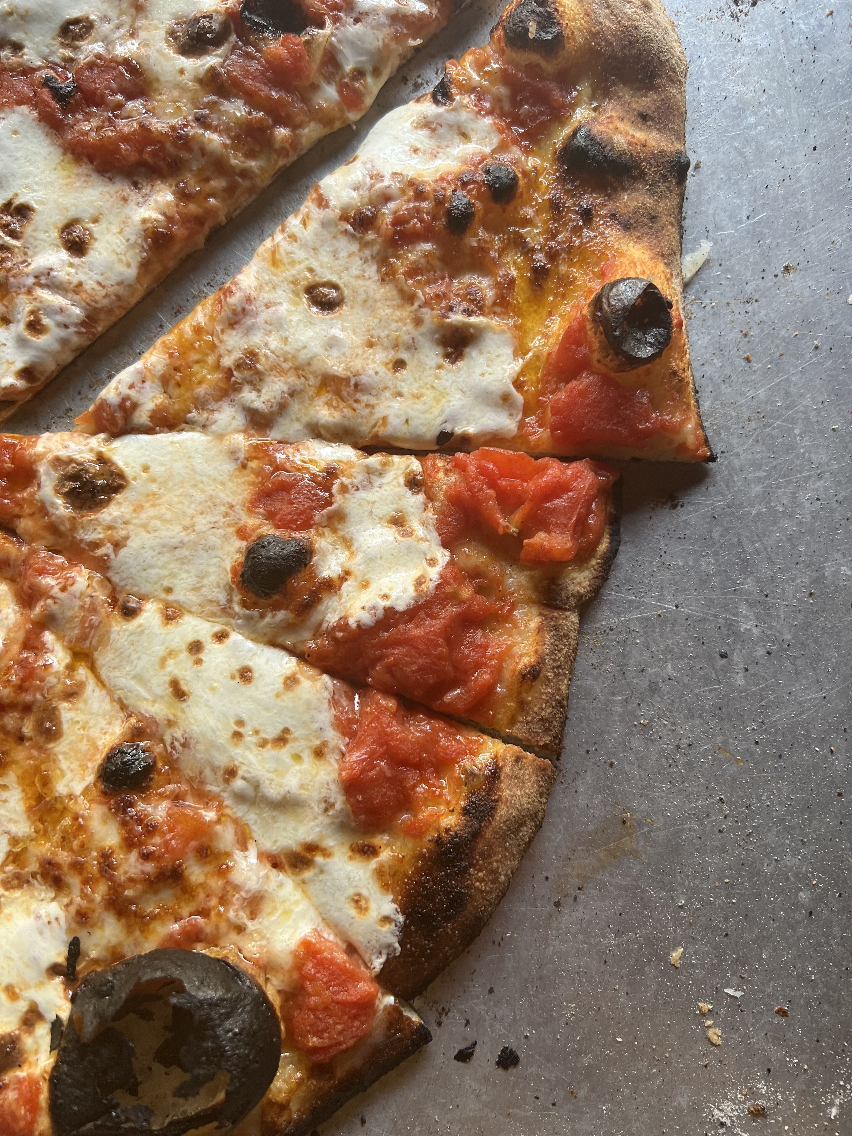 A pizza with burnt spots and melted cheese on a metal surface.