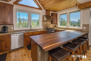 Un'ampia cucina con mobili in legno, una grande isola con sgabelli, una lavastoviglie e ampie finestre con vista sulle montagne.