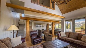 Ein großzügiges Wohnzimmer mit Ledersofas, einem Couchtisch und einer Chandelier. Eine Treppe führt in eine obere Ebene.
