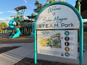 A sign welcoming visitors to S.T.E.A.M. Park, featuring a playground with slides and a solar panel structure.