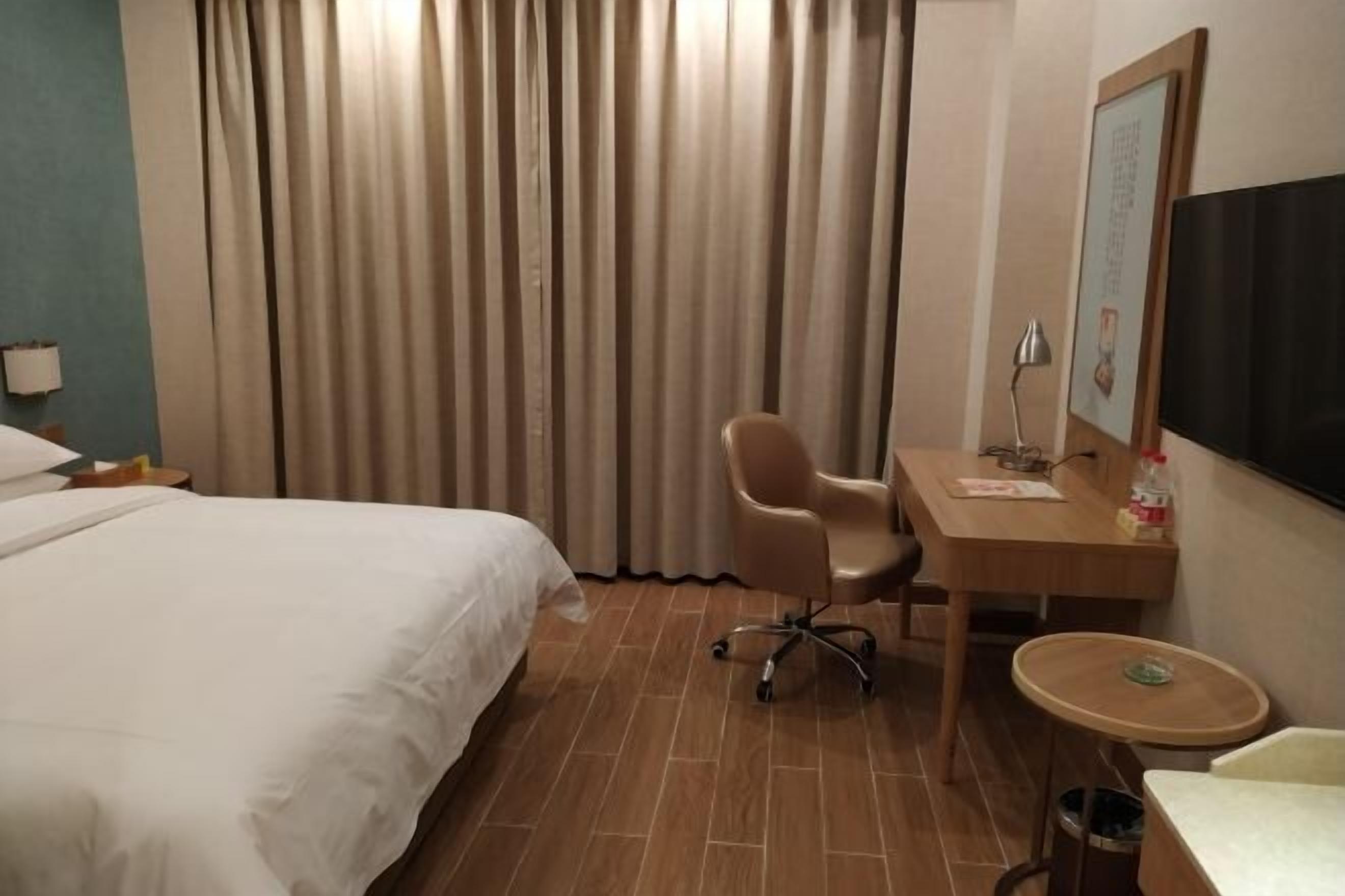 A hotel room with a bed, a desk, a chair, a TV, and a curtain.