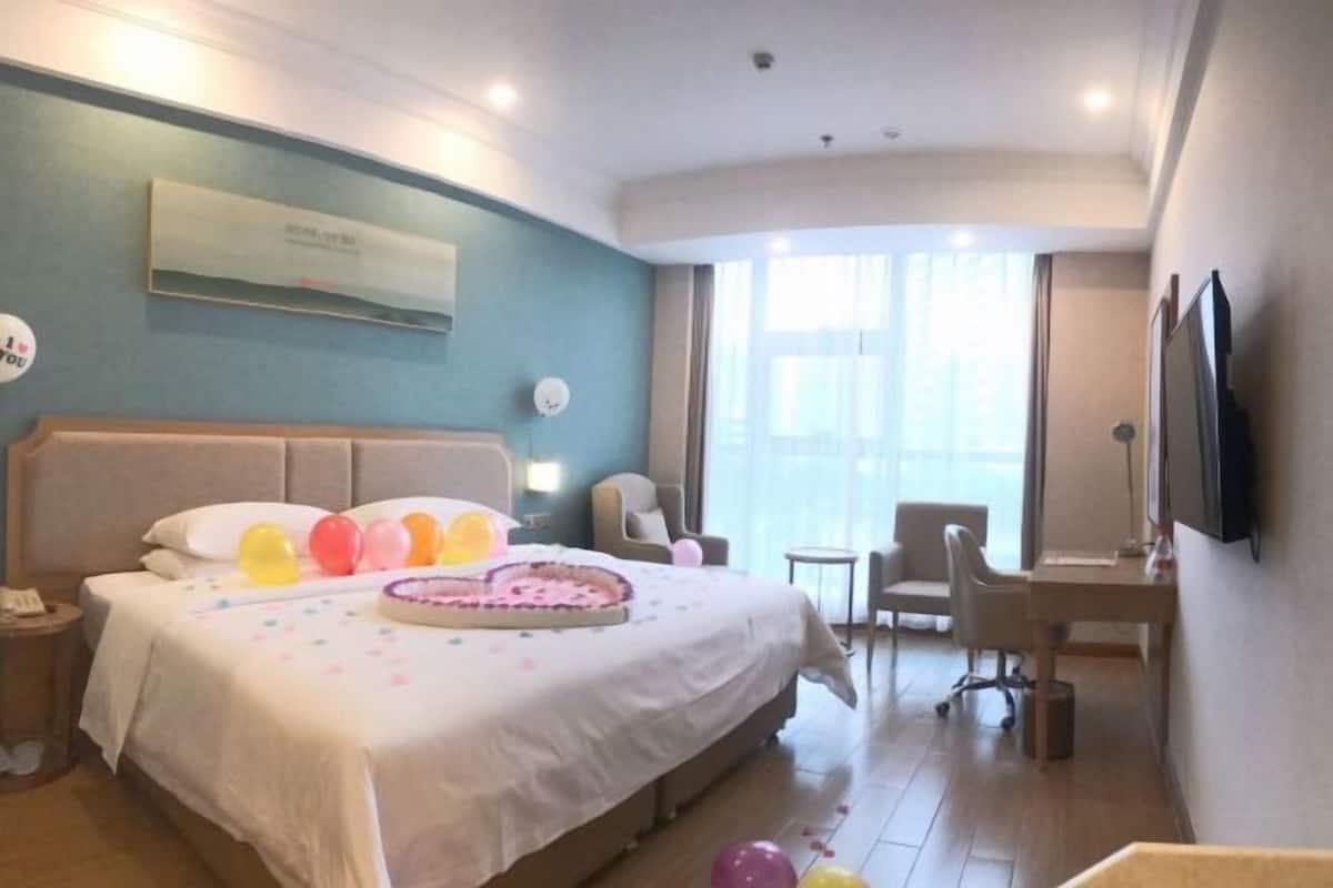 A hotel room with a bed, a desk, a chair, a TV, and a window.