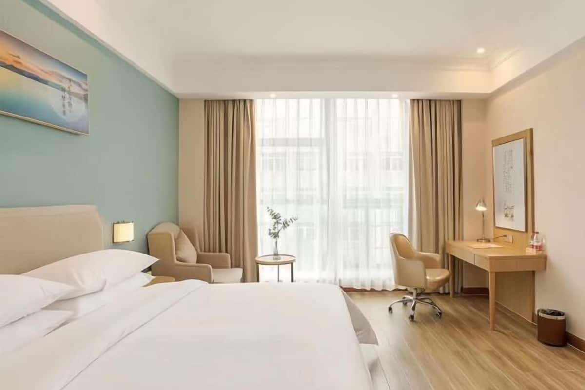 A hotel room with a bed, a desk, a chair, a small table, and a window with curtains.