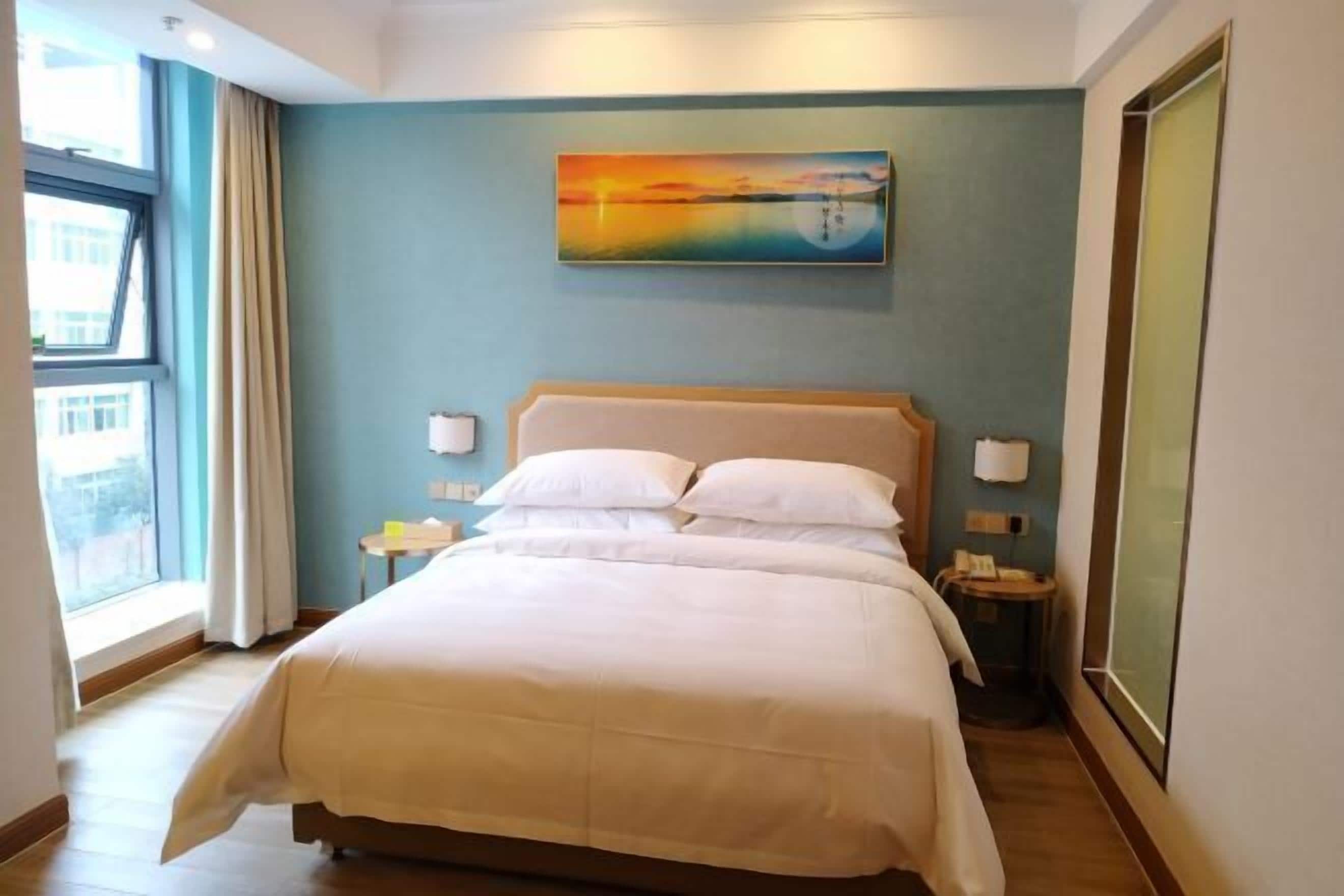 Una habitación de hotel con cama, un cuadro en la pared, una ventana y una mesita de noche.