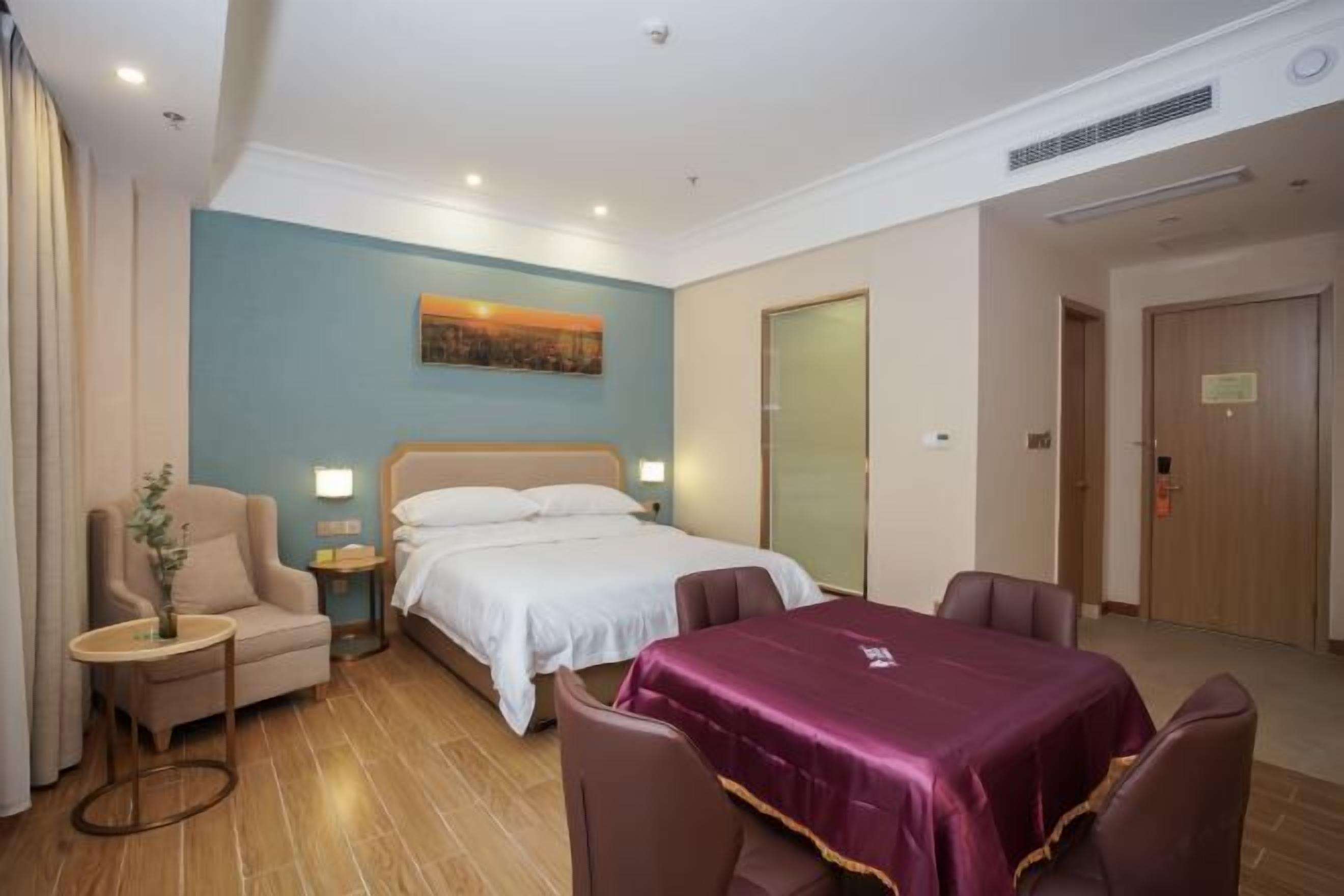 A hotel room with a bed, a desk, a chair, a table, and a painting on the wall.
