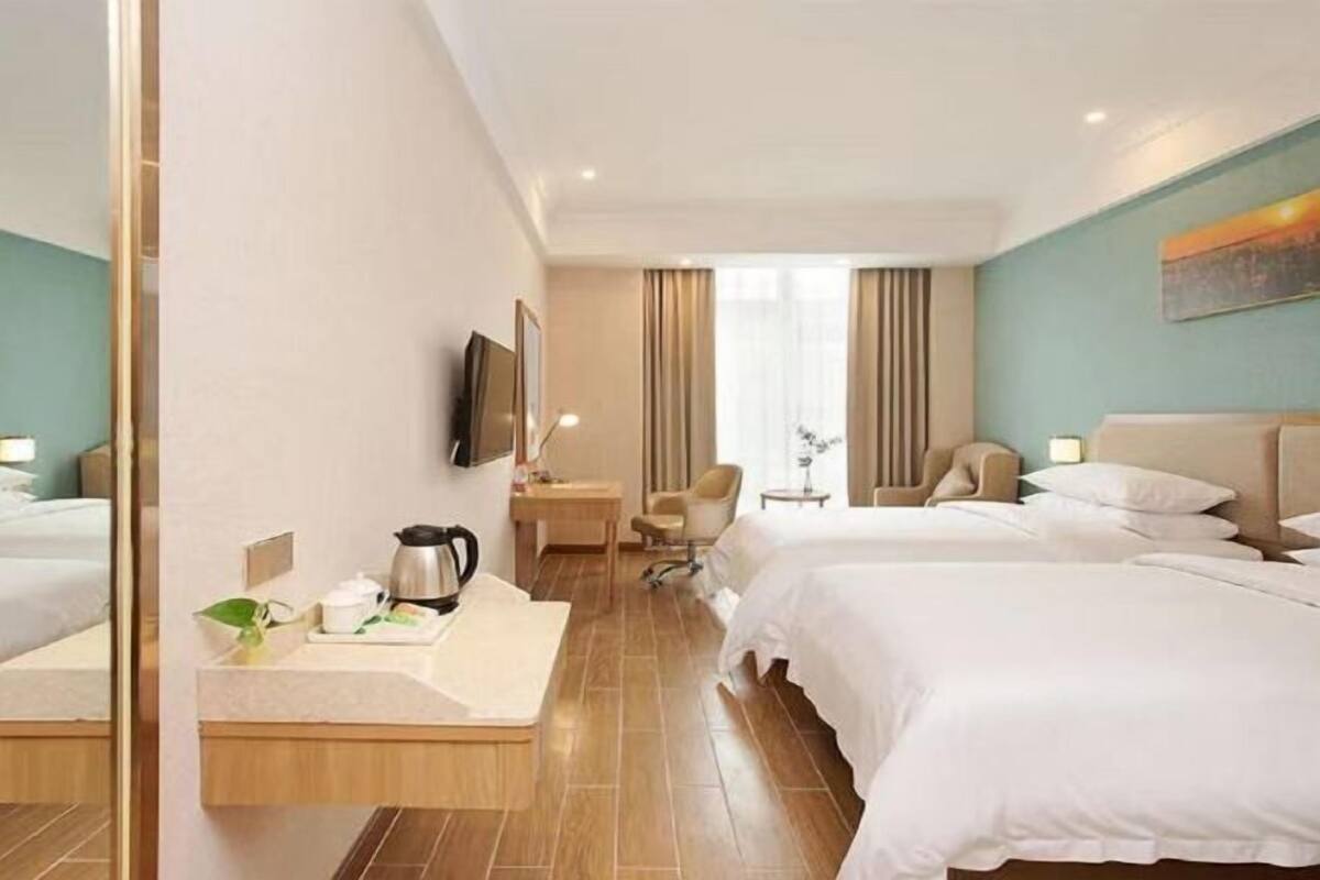 A hotel room with two beds, a desk, a chair, a TV, and a window with curtains.