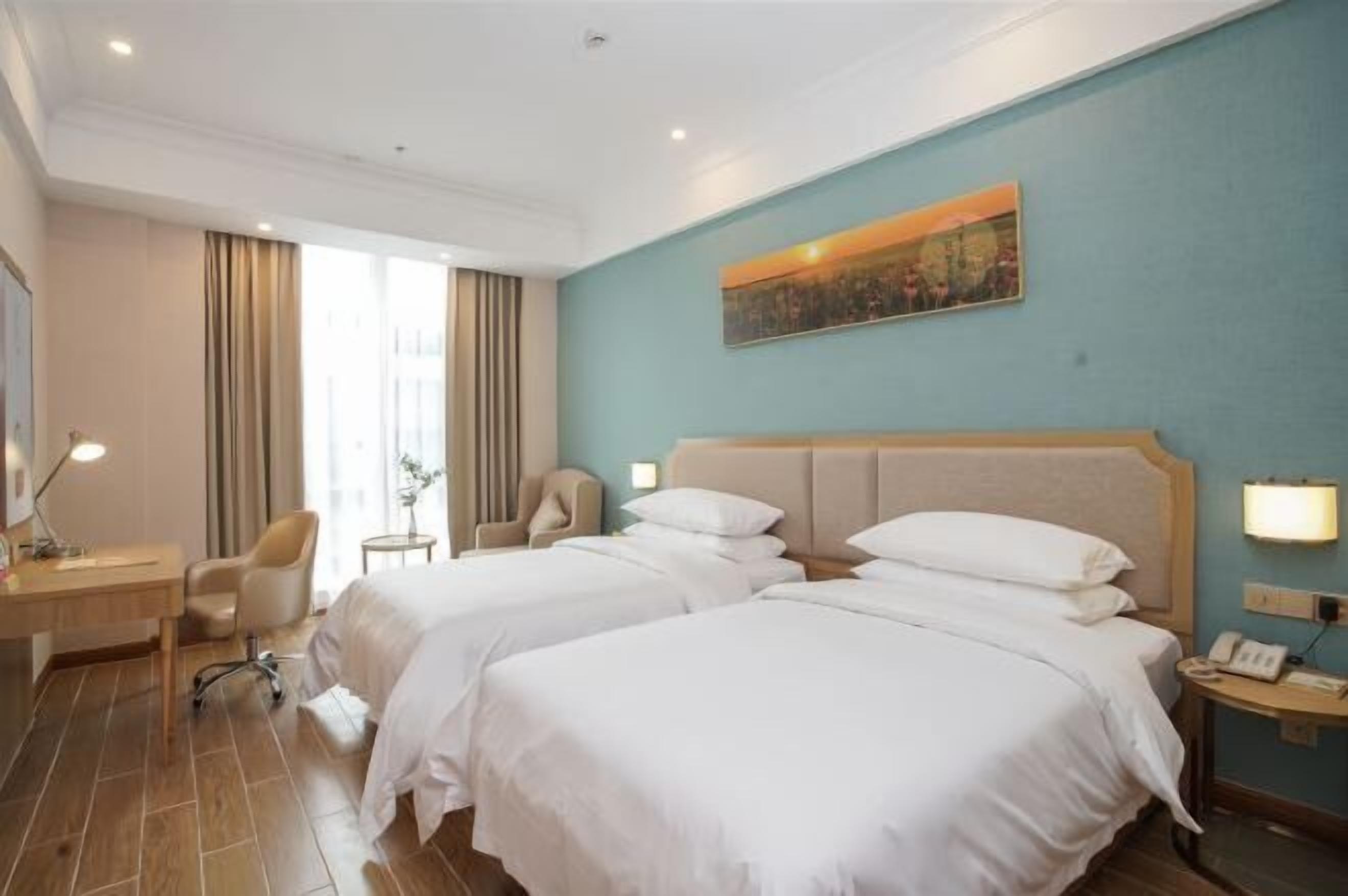 Habitación de hotel con dos camas, un escritorio, una silla, una lámpara y un cuadro en la pared.