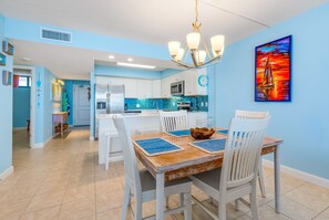A modern kitchen with white cabinets, a blue backsplash, and a dining area with white chairs and a wooden table. - Gulf Shores 504 Gorgeous fifth floor Beachfront View (Port Aransas)
