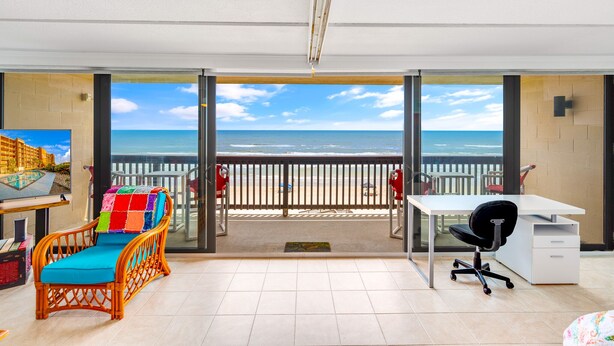 Een kamer met balkon, bureau, stoel en een kleurrijk kussen.