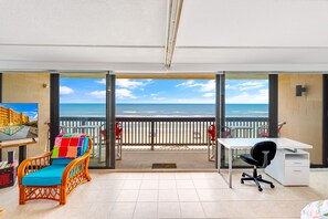 Et værelse med balkon, skrivebord, stol og farverig pude.