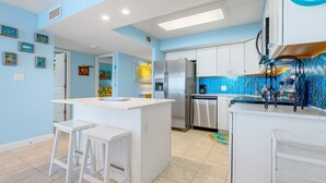 Een moderne keuken met een centraal eiland, roestvrijstalen apparatuur en een blauwe betegelde achterwand.