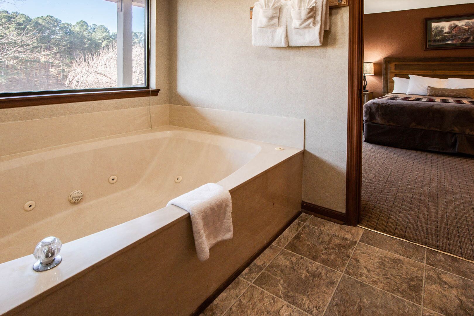 A bathroom with a large bathtub, a wooden headboard, and a view of trees through a window.