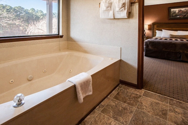 A bathroom with a large bathtub, a wooden headboard, and a view of trees through a window. - Fairways of the Mountains (Lake Lure)