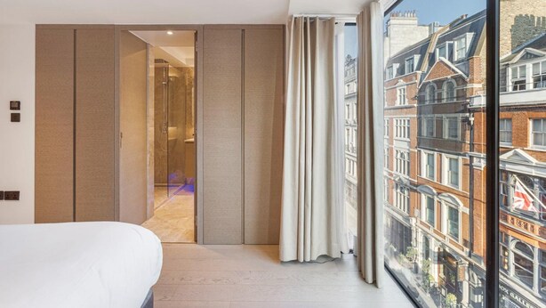 Une chambre d’hôtel dotée d’une grande fenêtre, d ’un lit, d’une porte coulissante et offrant une vue sur le paysage urbain.