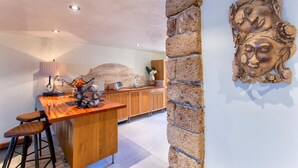 A kitchen with a wooden bar, stools, a stone accent wall, and a decorative wooden carving. - Cavour Loft in Alghero (Alghero)